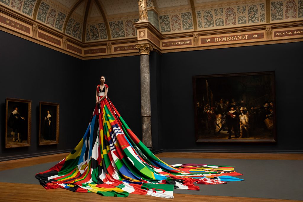 Valentijn de Hingh presents the Amsterdam Rainbow Dress in the Gallery of Honour at the Rijksmuseum Amsterdam, in front of Rembrandt’s iconic Night Watch. Image by Pieter Henket Studio.